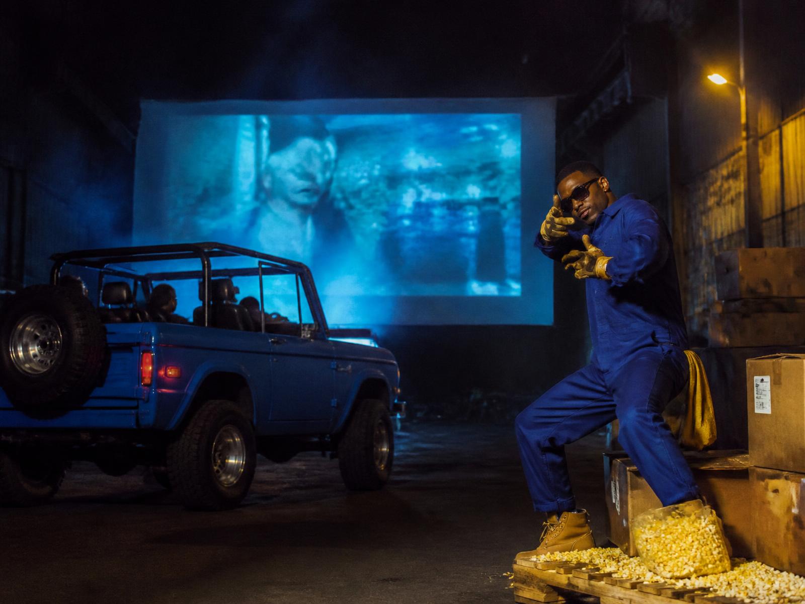 Chidi posing beside a blue off-road vehicle at a warehouse drive-in
